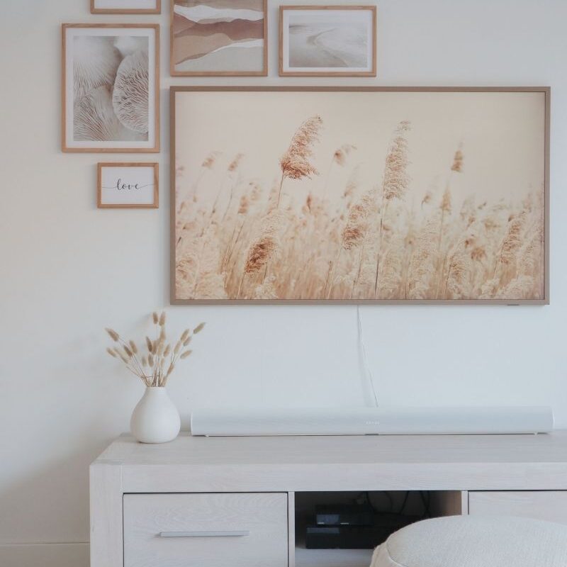 A gallery wall of light wood frames and neutral posters styled with the Samsung Frame TV